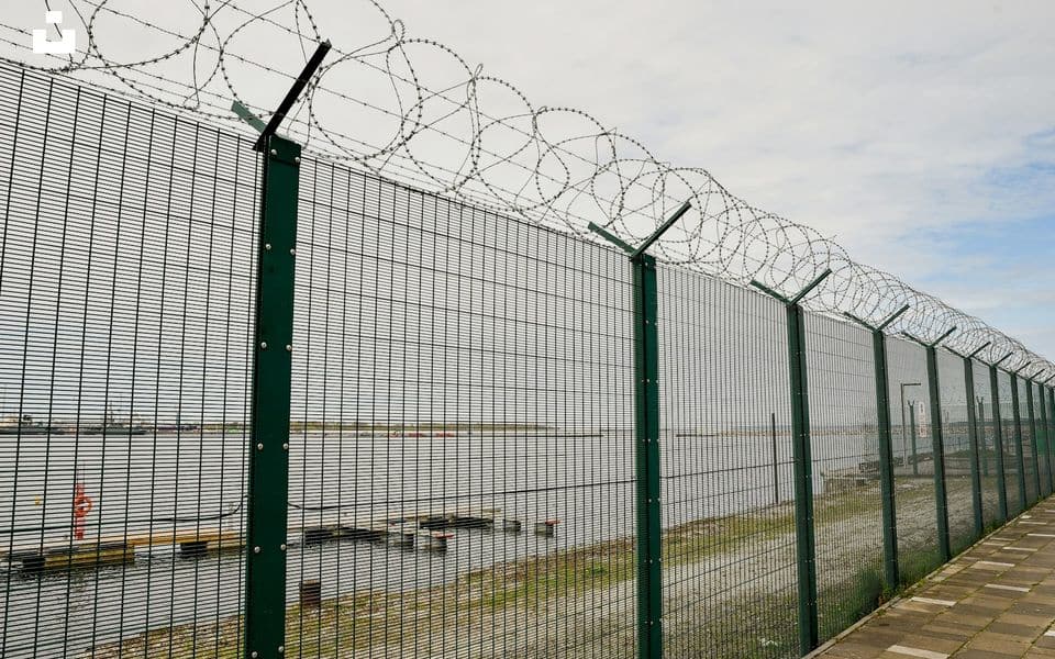 Tall high-security perimeter fence with barbed wire along the top