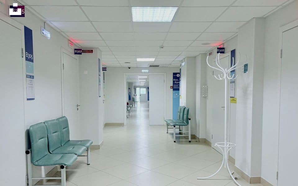 Pasillo de clínica hospitalaria limpia con puertas de habitaciones de pacientes y bancos